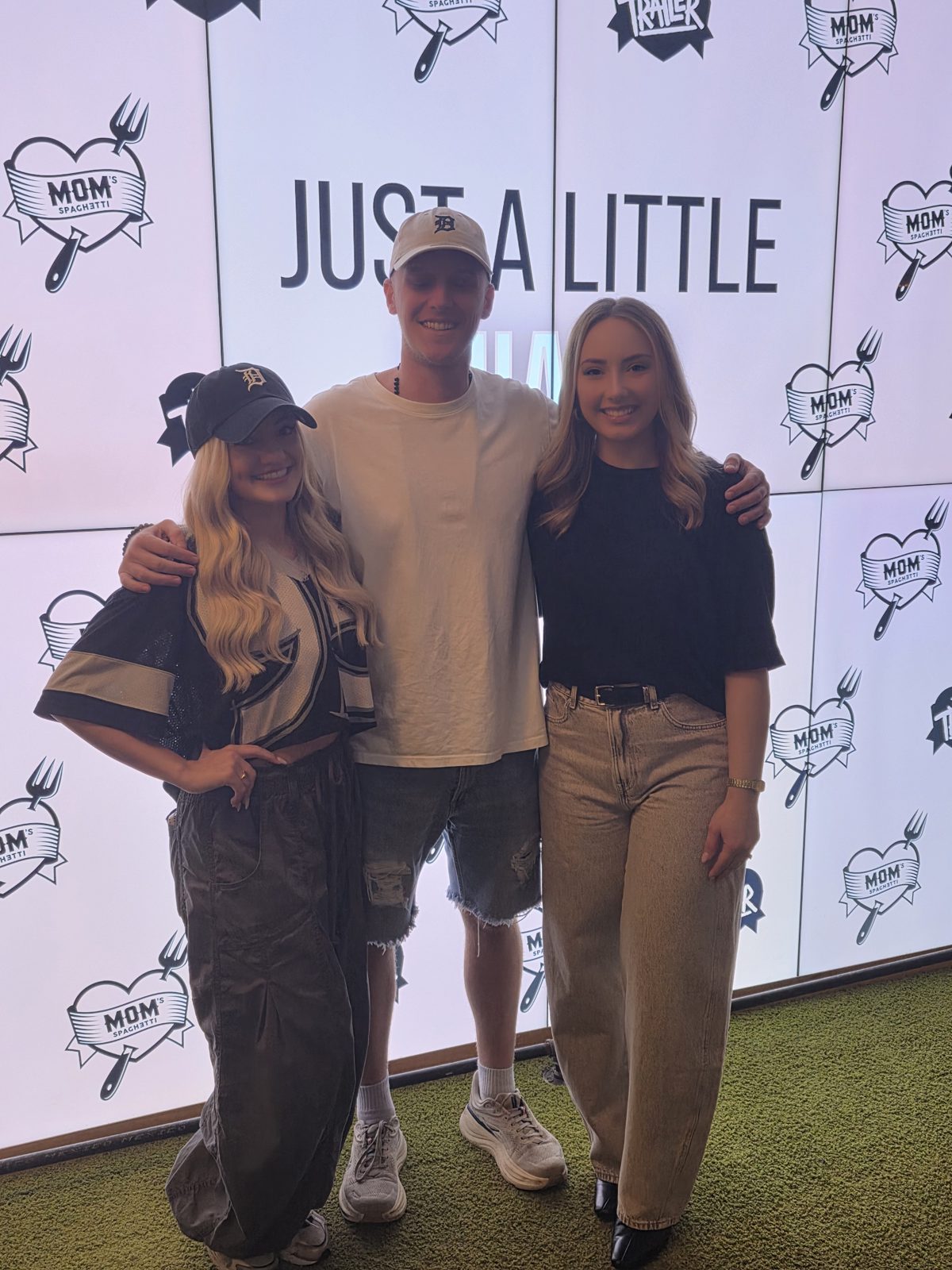 Brad Mines in a white tee and Tigers cap with Hailie Jade, in a black Tigers cap and jersey, and a friend in front of the Just a Little Shady video wall at Mom's Spaghetti in Detroit