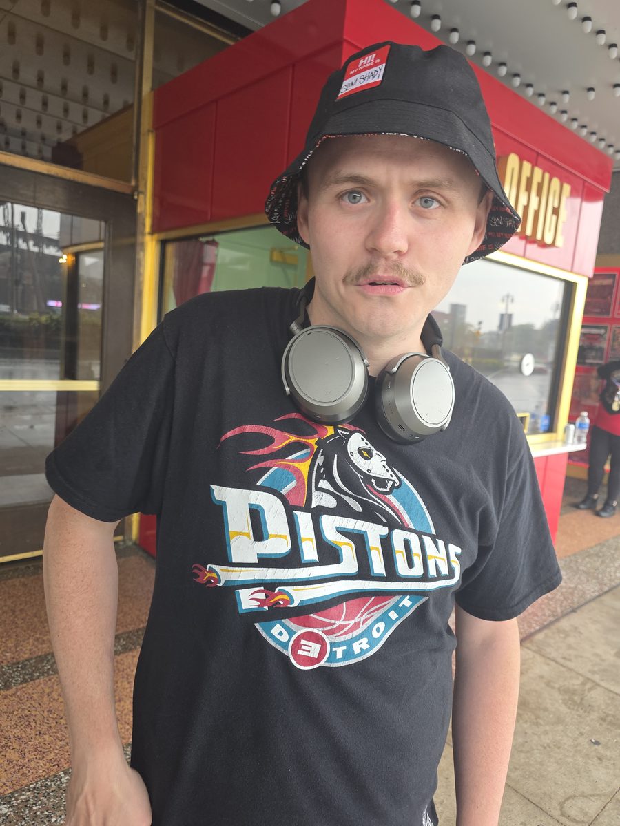 Brendan from the STANS documentary in a Detroit Pistons t-shirt, Slim Shady bucket hat and headphones, standing outside on Woodward Avenue in Detroit
