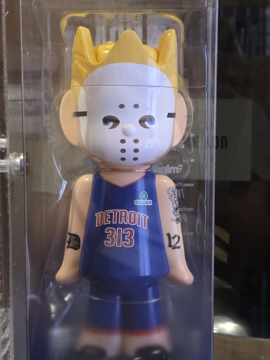 A boxed collectible vinyl figure of a crowned character in a hockey mask wearing a blue Detroit 313 basketball jersey, on display at The Trailer in Detroit