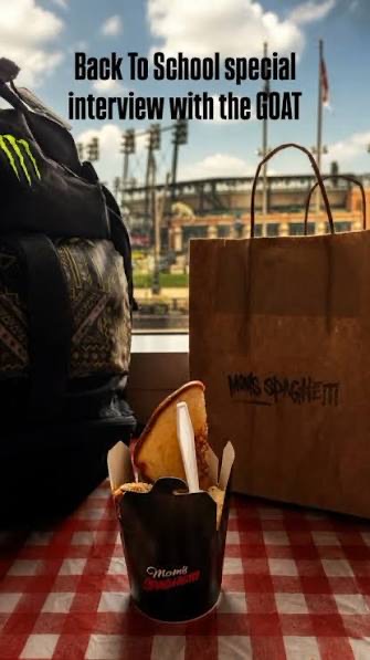 The iDstroy teaser: a vertical photo of Mom’s Spaghetti takeout — branded bag, noodle box and a S’ghetti sandwich — beside a backpack on a red-checked table, a ballpark visible across the street, captioned “Back To School special interview with the GOAT”