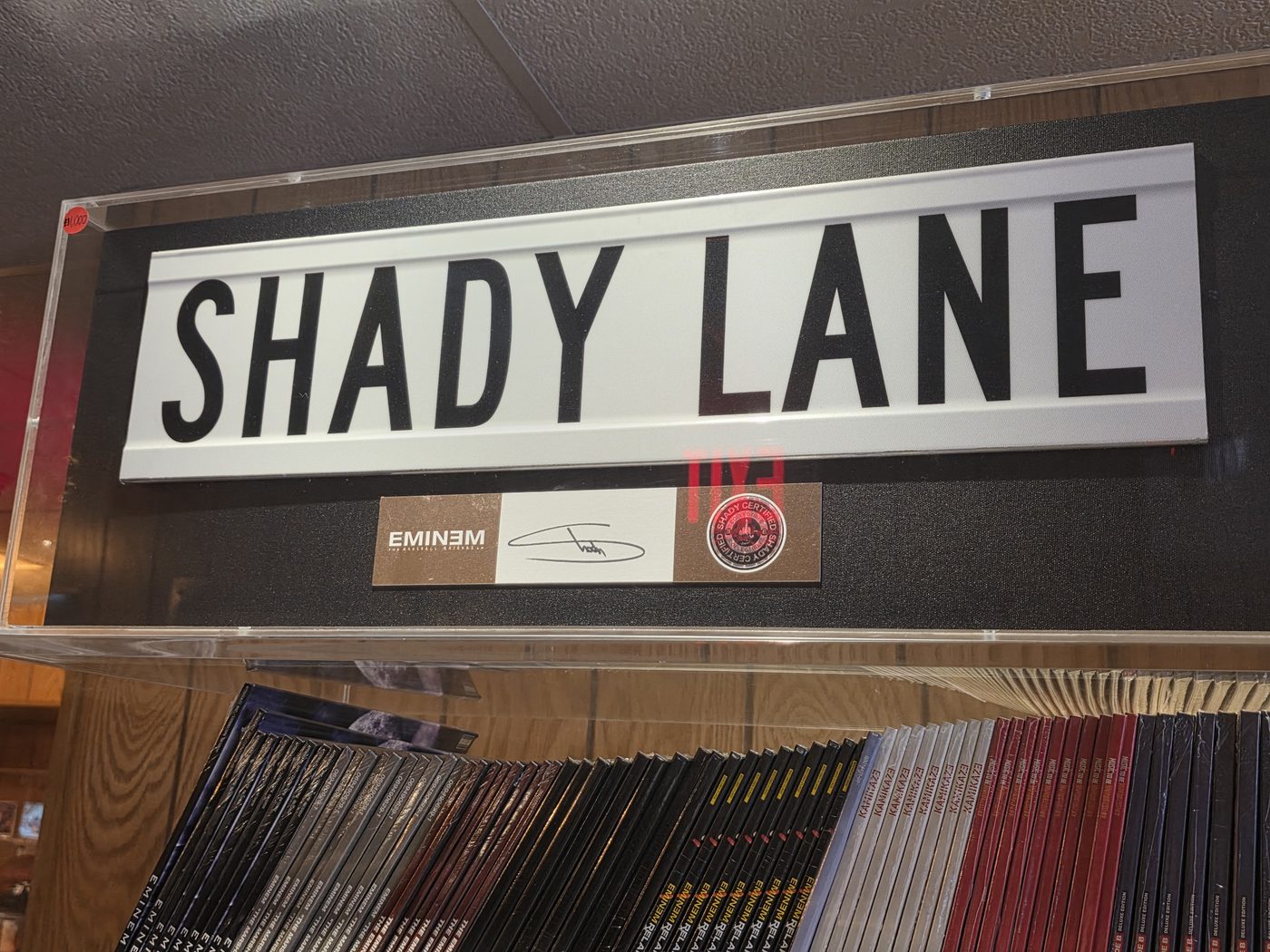 A large white SHADY LANE street sign in an acrylic display case at The Trailer in Detroit, with a signed Eminem authenticity plaque mounted below it